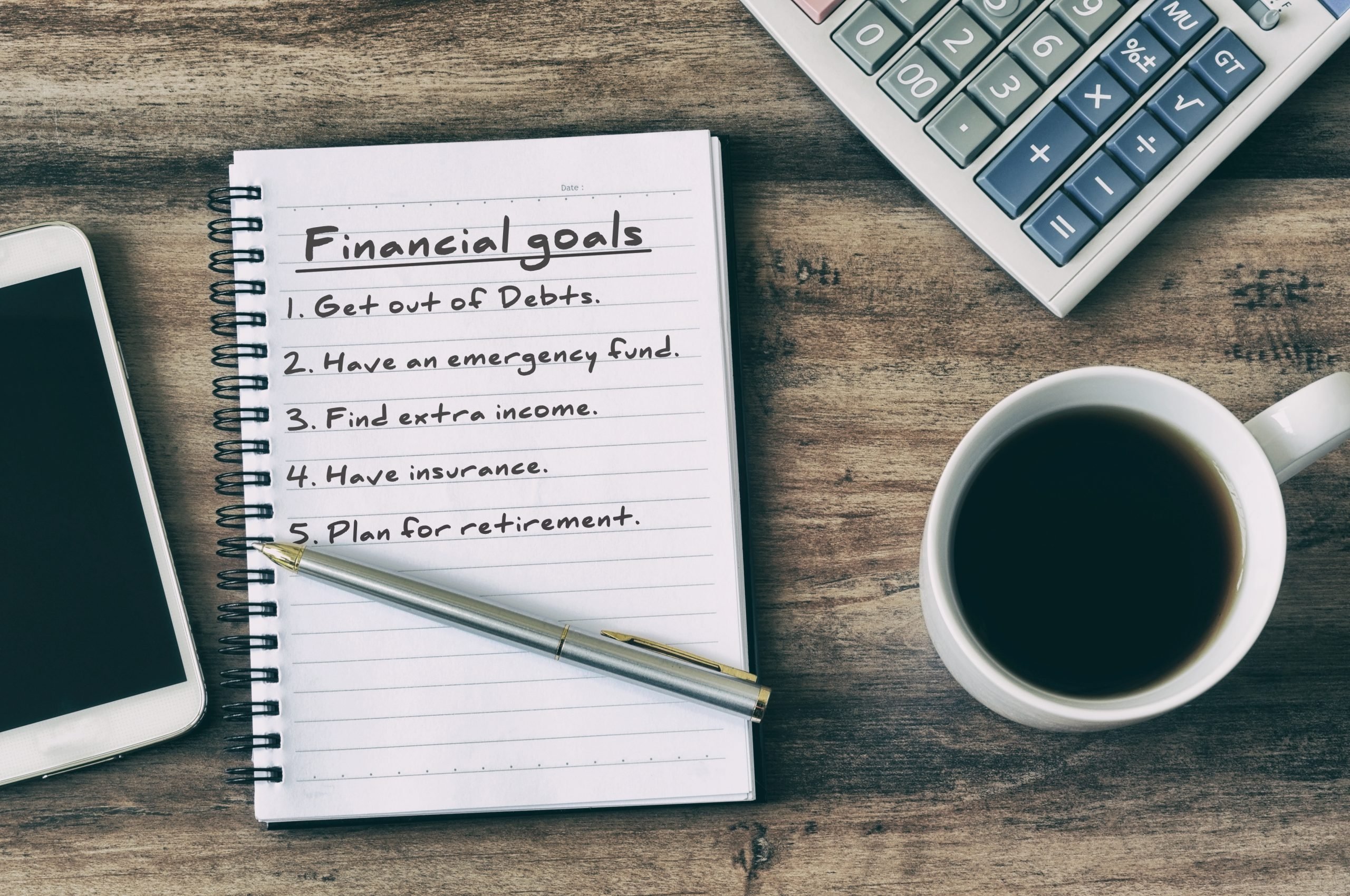 Financial goals on notepad on blank notepad with calculator, coffee, pen and smart phone on a wooden table, retro style.